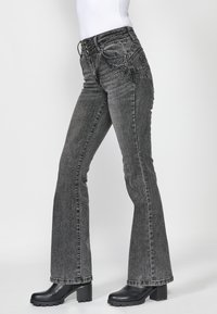 Jeans de campana negros con un talle medio, que presentan costuras decorativas en los bolsillos frontales y una tela de mezclilla texturizada.