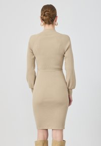 Beige ribbet strikket kjole med lange pufærmer, en struktureret halsudskæring og en tætsiddende talje. Designet har en længde til midt på læggen og en sømløs ryg.