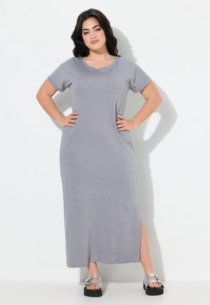 Vestido maxi gris con mangas cortas, cuello redondo, bolsillos laterales y una abertura lateral. Tela suave y corte relajado, combinado con sandalias de plataforma plateadas.