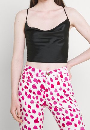 Top court en satin noir avec des fines bretelles, associé à un pantalon rose et blanc présentant un motif de cœurs irréguliers, mettant en valeur un design contrasté.