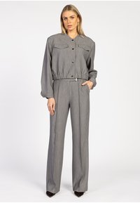 Grijze two-piece outfit met een col shirt met knopen en twee borstzakken, gecombineerd met een elastische tailleband en wijde broekspijpen.