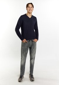 Marinblå v-ringad tröja, slim-fit grå jeans och grå sneakers. Tröjan har ribbade muddar; jeansen har en urtvättad finish som tillför textur.