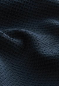 Tmavě modrý textil s texturovaným, tkaným vzorem. Měkké, mírně zmačkané záhyby látky vytvářejí hloubku a vizuální zajímavost.