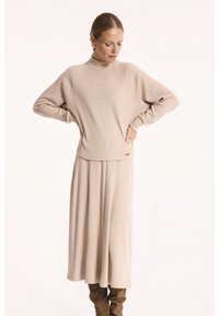Beżowy sweter prążkowany z kołnierzem typu funnel, w komplecie z dopasowaną długą spódnicą. Charakteryzuje się luźnym krojem oraz opadającymi szwami ramion.