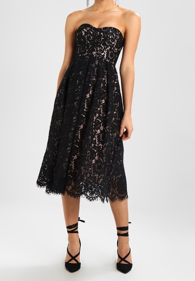 Musta pitsitoppi hihaton mekko, jossa on tiukka yläosa, levenevä puolipitkä helma, sakaroitu helmustus ja se on yhdistetty mustiin kenkään, joissa on remmejä.