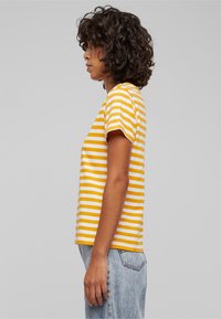 Gul og hvid stribet kortærmet t-shirt med en regular fit, lavet af blødt bomuld, parret med lyse vaskede denimjeans.