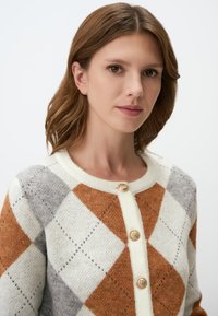 Cardigan à boutons en orange, gris et crème avec un motif argyle. Texture douce avec des boutons dorés et un col rond.