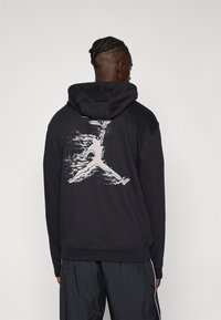 Sort hættebluse med et stort hvidt Jumpman-logo på ryggen. Lavet af et blødt stof med en afslappet pasform og snoretræk i hætten.