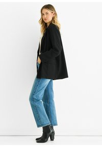 Black blazer with a relaxed fit, long sleeves, and front pockets paired with light blue straight-leg jeans and black heeled ankle boots.