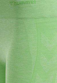 Grüne sportliche Leggings mit strukturiertem Finish, das ein dezentes Melange-Muster und Chevron-Details an der Seite aufweist. Logo in der Nähe des Bundes.