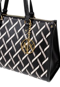 Sac à main noir avec un motif en chevron gris et crème, présentant un pendentif en logo doré, une fermeture à glissière et des poignées doubles. Finition en tissu texturé.