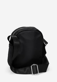 Bolso cruzado de tela negra con forma redondeada, cremallera plateada, correa ajustable y un bolsillo lateral. Textura suave con un diseño minimalista.