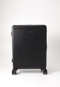Black hard-shell suitcase with four wheels, horizontal grooves on the surface, and a small logo plate on the front. Handle on the side.