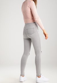 Grå smala jeans med sidodragkedjor, hög midja, gjorda av elastisk denim. Kombinerat med en ljusrosa ribbad tröja och vita sneakers.