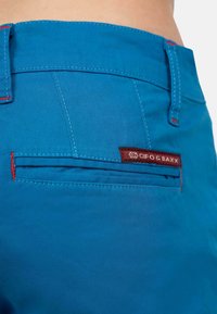 Blauwe shorts met een gladde textuur, voorzien van rode stiksels en een achterzak met een kastanjebruin label. Hedendaags ontwerp met een aansluitende tailleband.