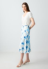 Gonna floreale in tessuto leggero con motivi di fiori blu e bianchi, abbinata a un top bianco a scollo a V semplice e sandali bianchi con tacco.