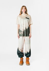 Camiseta de gran tamaño en crema y gris con textura, con un bolsillo negro en el pecho, combinada con pantalones holgados a juego que presentan un diseño degradado.