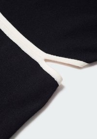 Gros plan d'un tissu noir avec une bordure blanche montrant une petite fente ou un détail découpé le long du bord.
