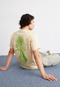 Camiseta de algodón color crema con un diseño floral verde en la parte posterior. Mangas cortas, corte cómodo y escote redondo.