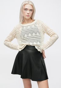 Maglione aperto di maglia color crema con motivi geometrici e scollatura rotonda, abbinato a una gonna nera in pelle a ruota.