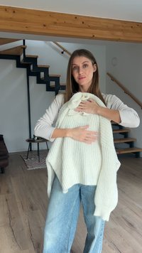 Pulover tricotat gros, de culoare crem, ținut în mâini, cu croială lejeră și textură ribată. Material moale, cu detalii vizibile ale cusăturilor.