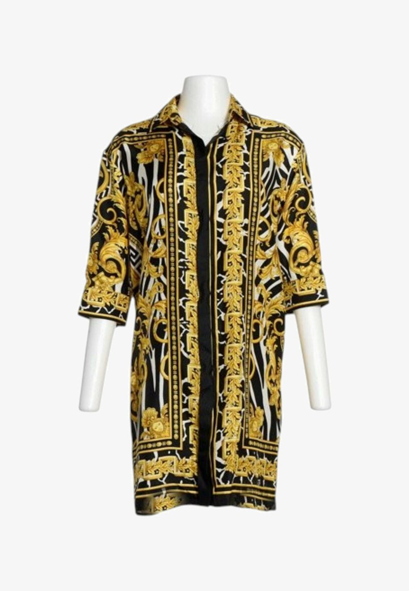 Chemise longue à motif noir et or avec manches trois-quarts et col, présentée sur un torse de mannequin avec un fond blanc.