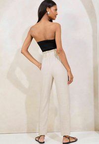 Pantalones de lino beige de cintura alta con una cinturilla plisada, combinados con un top negro sin mangas y sandalias planas negras.