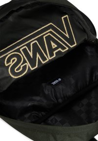 Interno di uno zaino in tessuto verde con un grande logo ricamato "VANS" in oro. Fodera nera a motivo con un'etichetta visibile.