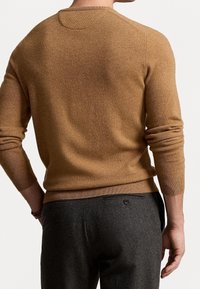 Brun tröja med en mjuk textur, rundad hals och åtsittande ärmar, i kombination med mörkgrå byxor som har sidofickor och knappdetaljer.