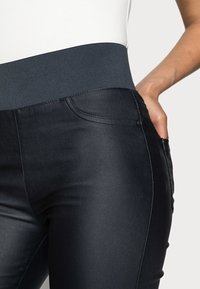 Högmidjade svarta denimleggings med en ruggad grå midja, som har framfickor och en slät, elegant yta.