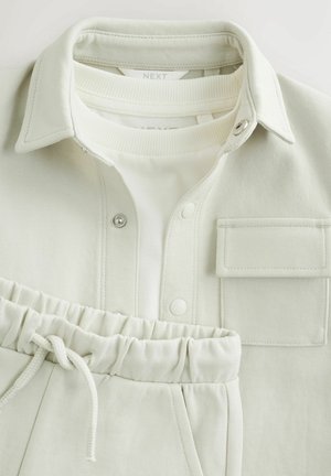 Heleroheline sobiv komplekt, mis koosneb kraega särkist, millel on trukknööbid ja rinnatasku, ning elastse vöökohaga pükstest. Sile tekstuur.