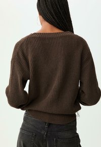 Pull en tricot marron avec une coupe ample, un ourlet côtelé et des manches larges. La texture est épaisse, ajoutant de la profondeur au design.