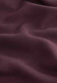 Tejido de algodón burdeos con una textura suave y líneas sutiles, que muestra pliegues y arrugas suaves. Ideal para ropa o tapicería.