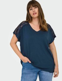 Navy blue short-sleeve top with V-neck and lace accents on shoulders, crafted from soft fabric, paired with light blue jeans.