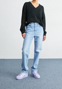 Černý pletený svetr s výstřihem do V a otevřeným pletením, spárovaný se světle modrými džíny rovného střihu a fialovými teniskami Adidas.