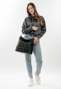 Black quilted handbag with a shiny finish, featuring a structured shape and a top handle. Worn with a gray hoodie and light blue jeans.