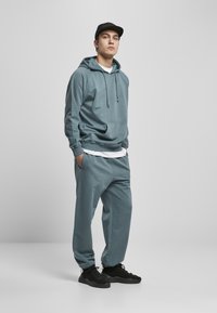 Hoodie blu chiaro con tasca a marsupio e coulisse, abbinato a pantaloni della tuta coordinati. Sneakers nere. Texture del tessuto liscia e casual.