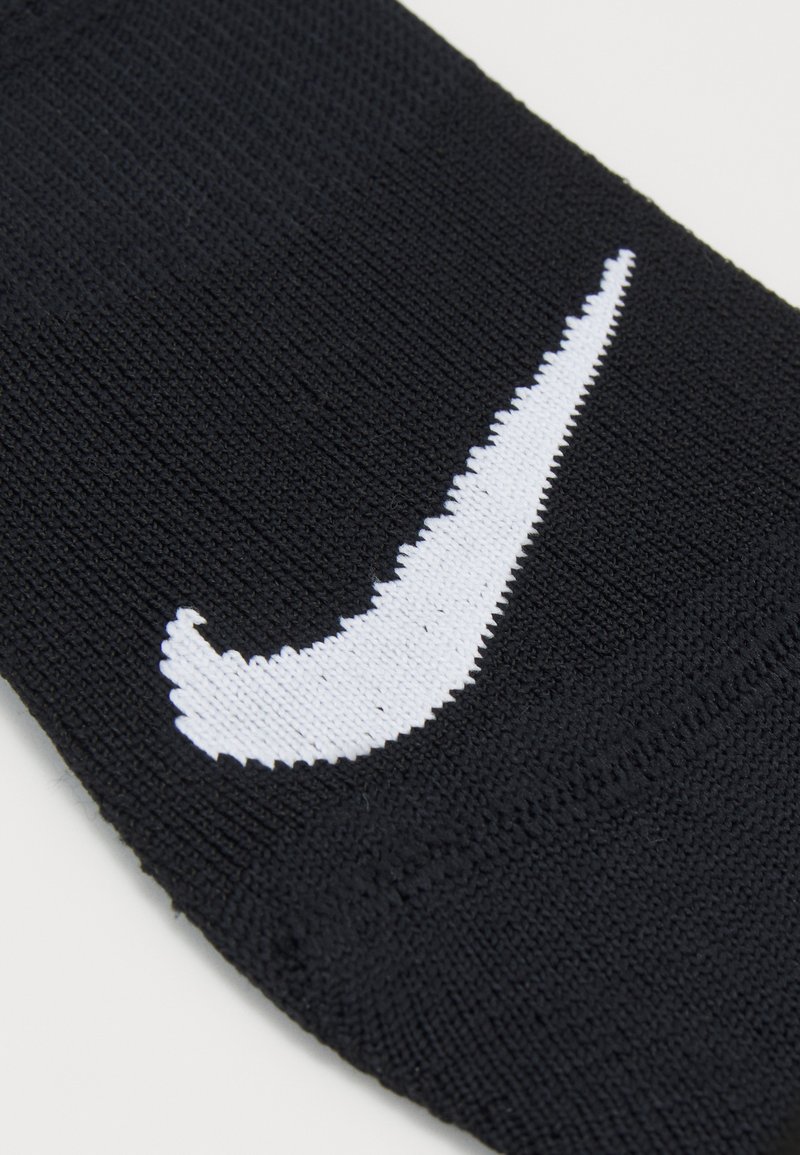 Svart idrottssocka gjord av texturerat tyg, med en framträdande vit Nike-swoosh-logotyp. Enkel design utan ytterligare mönster.