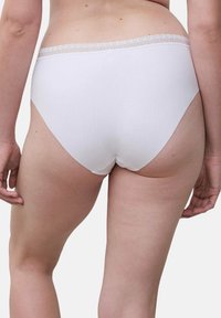 Woman from the back wearing plain white full-coverage underwear with lace trim on the waistband against a white background.
