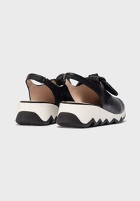 Sandalias de cuero negro con talones abiertos, puntas redondeadas y suelas blancas con zigzags. Cuentan con una correa en el tobillo para un ajuste seguro.