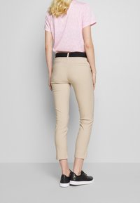 Beżowe spodnie o kroju slim, sięgające do połowy łydki, z tylnymi kieszeniami, w połączeniu z jasnoróżowym t-shirtem z wzorem oraz czarnymi tenisówkami.