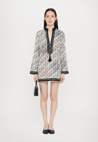 Rochie scurtă dintr-un material transparent alb și negru cu un model geometric, având un decolteu înalt, mâneci lungi și o margine neagră.