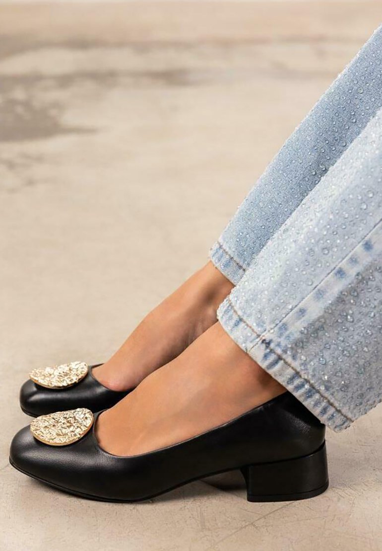 Zapatos de tacón cuadrado de cuero negro con puntera redonda y adornos texturizados dorados en la parte frontal. Llevados con jeans de longitud hasta el tobillo de color azul claro.