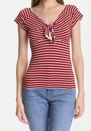 Punavalkoraidallinen paita, jossa on lyhyet hihat, V-aukko ja edessä solmimisyksityiskohta. Valmistettu pehmeästä kankaasta ja istuvalla mallilla. Yhdistetty sinisiin farkkuihin.