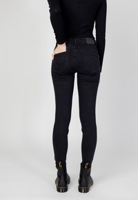 Jeans skinny in denim nero con vita a media altezza, dotati di tasche posteriori e dettagli di cucitura discreti, abbinati a stivaletti neri alla caviglia.