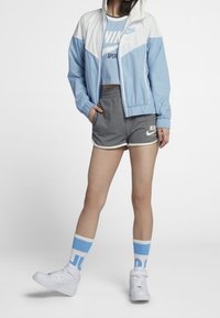 Light blue windbreaker with a white upper section, gray shorts with white trim, white high-top sneakers, and blue striped socks.