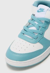 Sneaker Nike avec une tige en cuir blanc et bleu clair, une boîte à orteils perforée et des lacets plats. Accentué d'un logo bleu sur la languette.