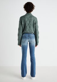 Green knitted sweater with a textured wave pattern, paired with light blue flared jeans featuring a faded look and back pockets.