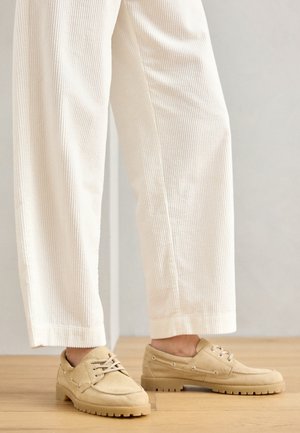 Zapatos de ante beige con punta redonda, cordones y suelas de goma gruesas, combinados con pantalones de pana blancos.