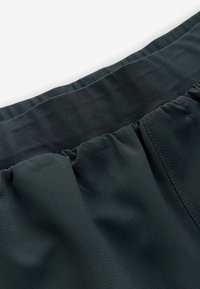 Mørkegrønne shorts har en tekstureret talje og en sammensnøret kant. Stoffet har et rutenetmønster med en glat tekstur og ensartet syning.